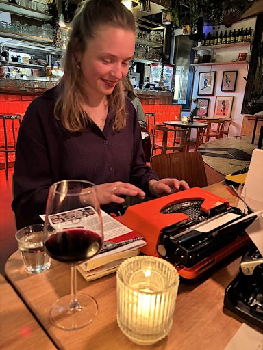 Jonge vrouw achter typemachine met een glaasje wijn