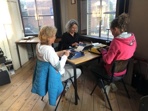 Drie vrouwen zitten aan een tafel en werken aan hun laptops in een lichte ruimte.