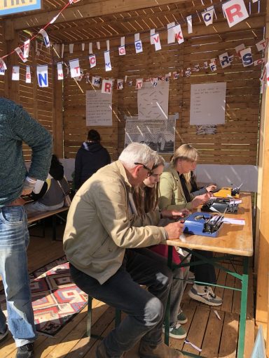 Twee mensen zitten aan een tafel in een houten hut, bezig met knutselen.