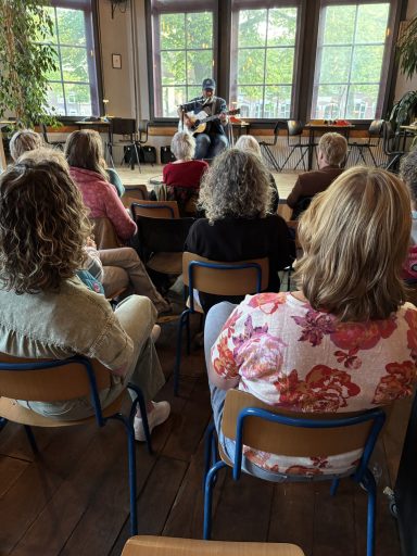 Mensen zitten op stoelen en luisteren naar muzikanten tijdens een intieme optreden.