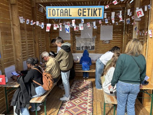 Een houten tent met mensen die aan tafels zitten en informatie ophalen.